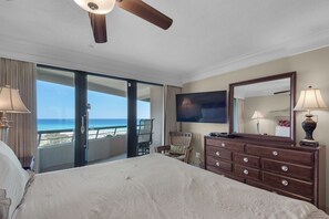 A hotel room with a bed, a dresser, a television, and a balcony with a view of the beach. - Edgewater Beach Condo 0603 (Destin)