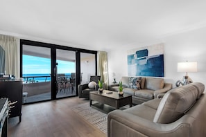 A modern living room with a sofa, coffee table, and a view of the ocean through large sliding doors. - Edgewater Beach Condo 608 (Destin)
