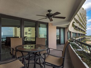 A balcony with a glass door, a table with chairs, and a ceiling fan. - Edgewater Beach Condo 1107 (Destin)