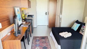Een kleine kamer met een bed, een bureau en een klein kitchenette.