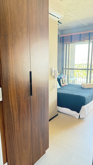 Een kamer met een houten garderobe, een bed met een blauwe sprei, een telefoon en een raam met jaloezieën.