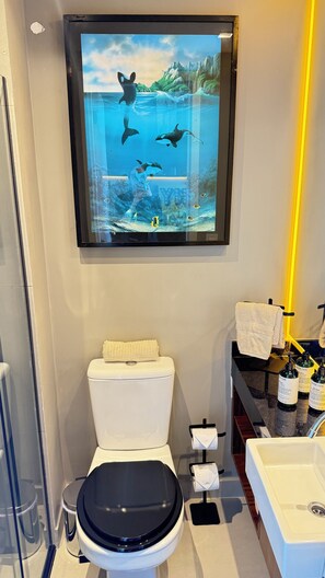A modern bathroom with a toilet, sink, and a wall-mounted TV displaying an underwater scene. - Apartment with beautiful views of the gardens. (São Paulo)