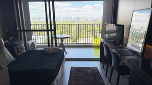 A hotel room with a bed, a desk with a computer, a TV, and a balcony with a city view. - Apartment with beautiful views of the gardens. (São Paulo)
