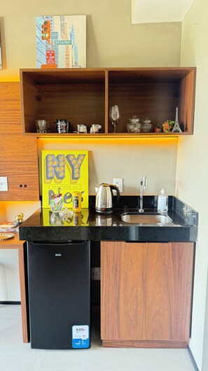 A compact kitchen with a black refrigerator, wooden cabinets, and a countertop with a coffee maker and kettle. - Apartment with beautiful views of the gardens. (São Paulo)