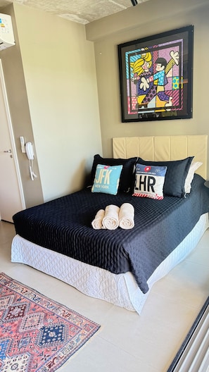 A hotel room with a bed, two pillows, a framed artwork, a telephone, and a patterned rug. - Apartment with beautiful views of the gardens. (São Paulo)