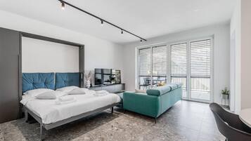 Un dormitorio moderno con cama, sofá, escritorio y un ventanal con persianas.