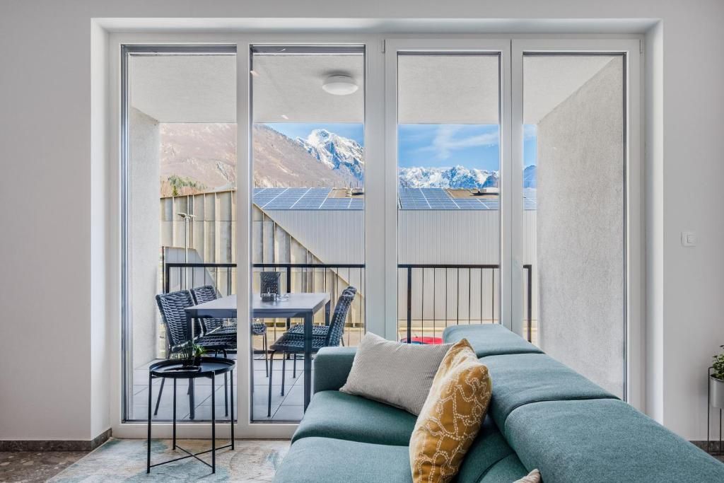 Un soggiorno moderno con un divano, un tavolo e sedie, una porta vetrata scorrevole che dà su un balcone con vista sulle montagne e pannelli solari.