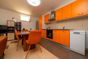 A modern kitchen with orange cabinets, a dining table with chairs, a built-in oven, and a dishwasher. - Casa delle Rondini in Belej (Belej)