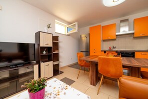 A modern kitchen with orange cabinets, a dining area with a wooden table and orange chairs, a television, and a small plant on the counter. - Casa delle Rondini in Belej (Belej)