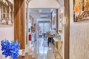 A hallway with a kitchen area, a dining table, and chairs. There is a fire extinguisher on the wall, and a vase with flowers on the floor. - Beautiful, private 3BR Sliema House w/Roof Terrace (Sliema)
