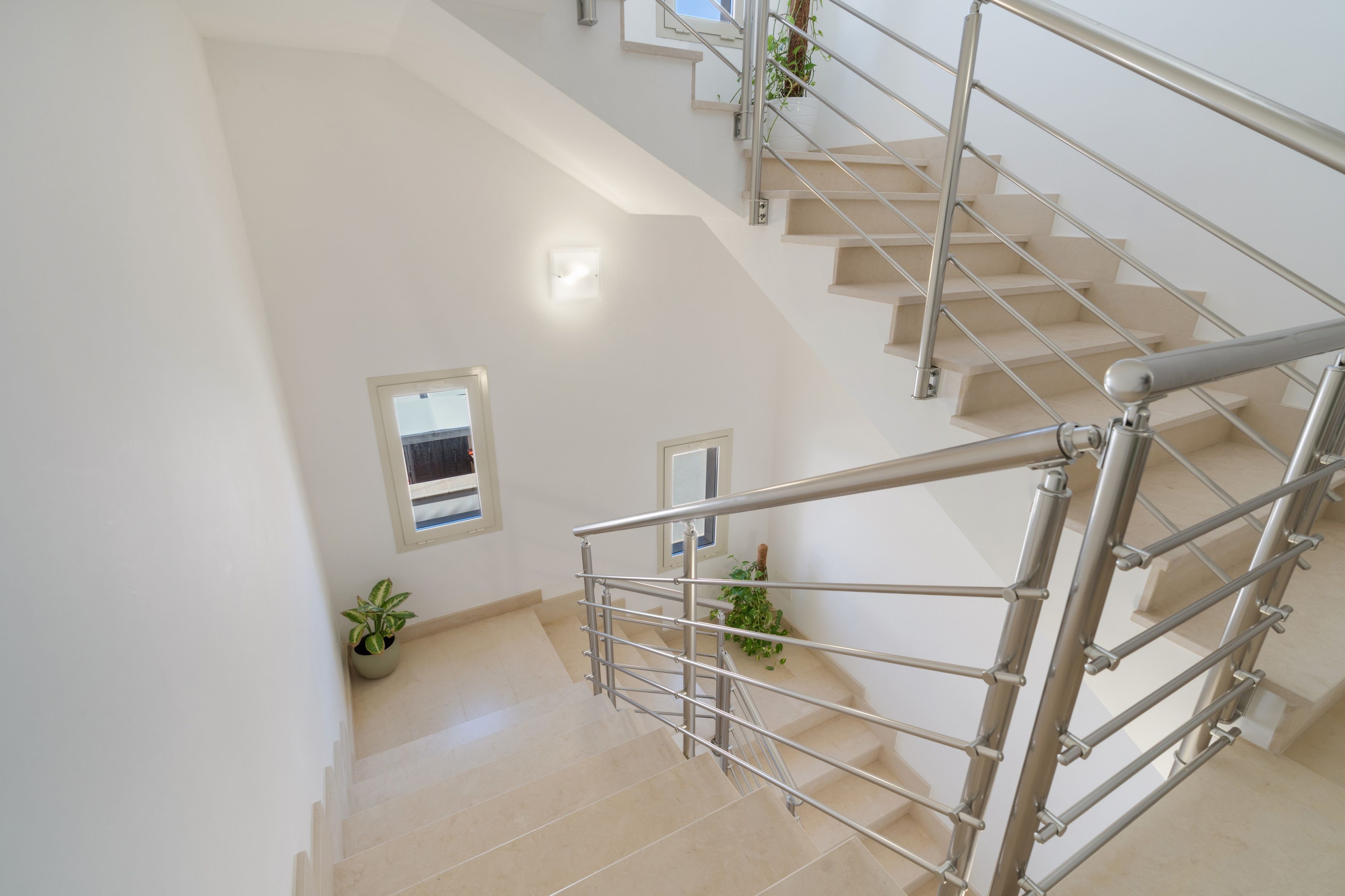 Un escalier moderne avec des rampes en métal et des marches de couleur beige, menant à l’étage supérieur.