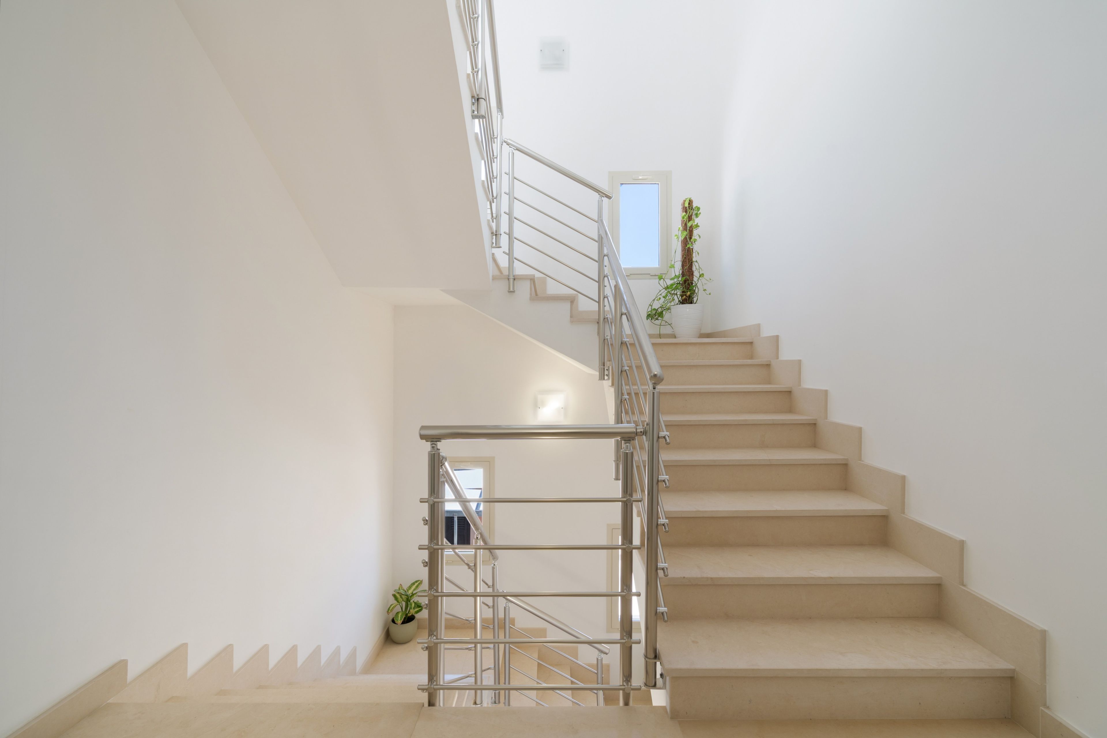 Un escalier avec une rampe métallique, des marches de couleur beige et des plantes en pot au sommet.