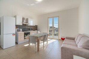 A modern kitchen with a dining table and chairs, a red chair, and a balcony with a view. - Apartment 'Lungomare Avola  with Sea' with Balcony, Wi-Fi and Air Conditioning (Avola)
