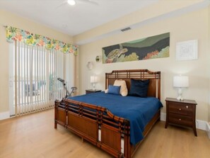 A bedroom with a wooden bed, two bedside tables, a window with blinds, and a painting on the wall. - Waterfront Condo In Placida (PLACIDA)