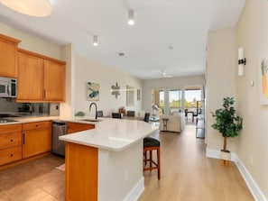 A spacious kitchen with wooden cabinets, a central island, and a dining area with a view. - Waterfront Condo In Placida (PLACIDA)