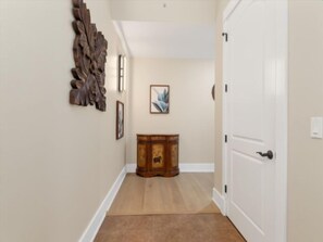 A hallway with a wooden floor, a white door, and a wooden cabinet with a picture on top. - Waterfront Condo In Placida (PLACIDA)