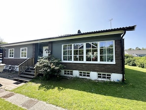 Ett enplanshus med en veranda framtill, en trappa som leder upp till entrén och en välskött gräsmatta.