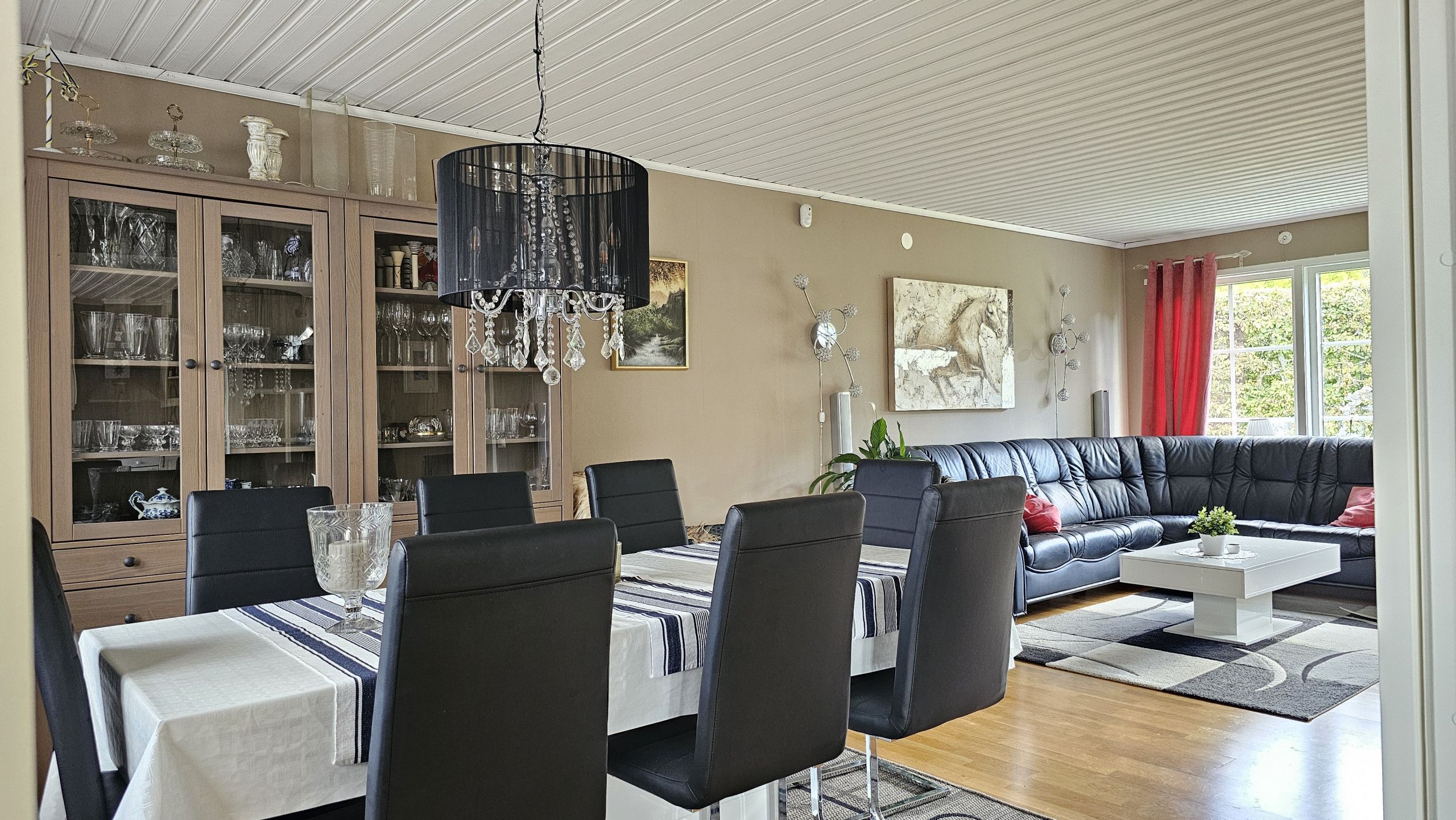 En matplats med ett bord dukat för fyra personer, omgiven av stolar, och en svart soffa i vardagsrummet.