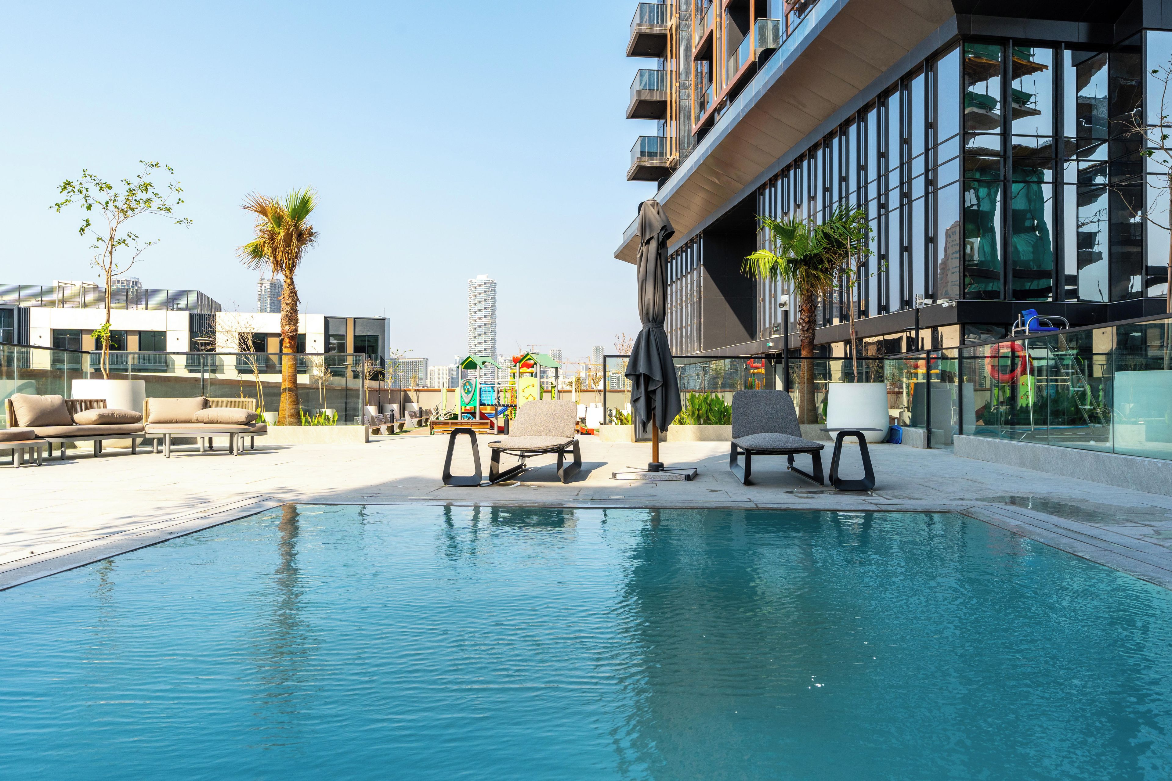 Zona de piscina con sillones de descanso y un edificio moderno con amplios ventanales.