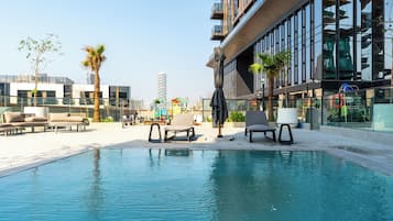 Zona de piscina con sillones de descanso y un edificio moderno con amplios ventanales.