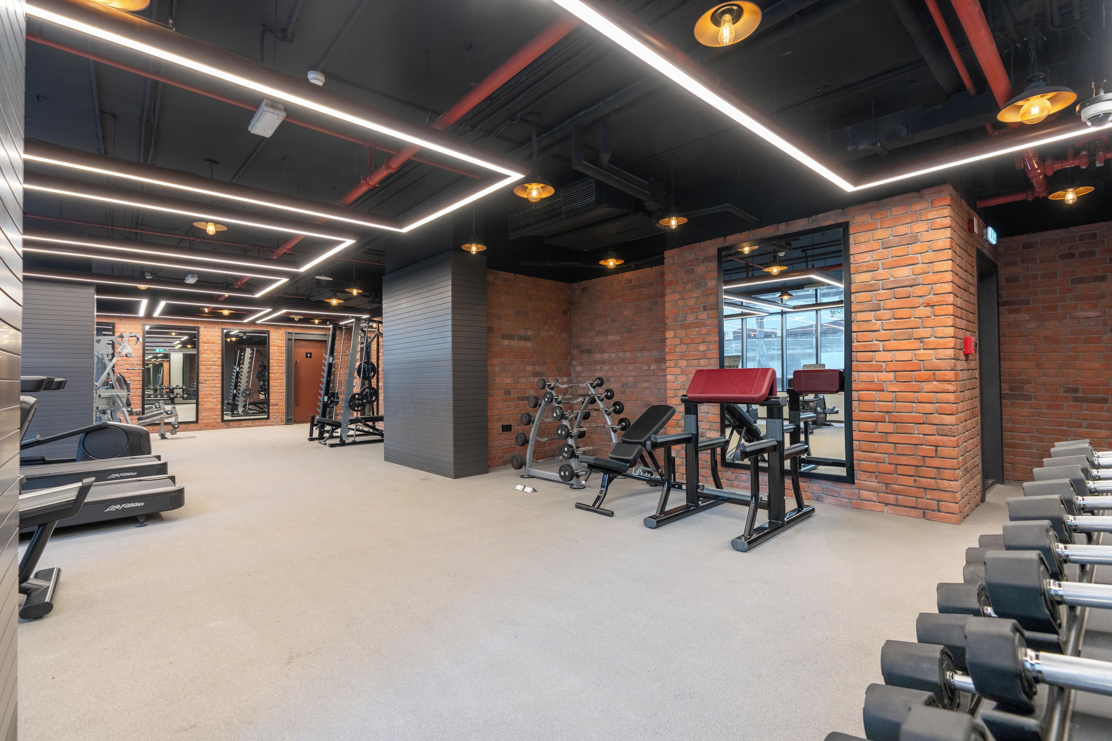 Un gimnasio con equipamiento de ejercicio, una pared de ladrillo y un ventanal grande.