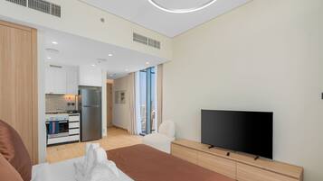Habitación de hotel moderna con cama, televisor de pantalla plana, cómoda de madera y una zona de cocina con refrigerador.
