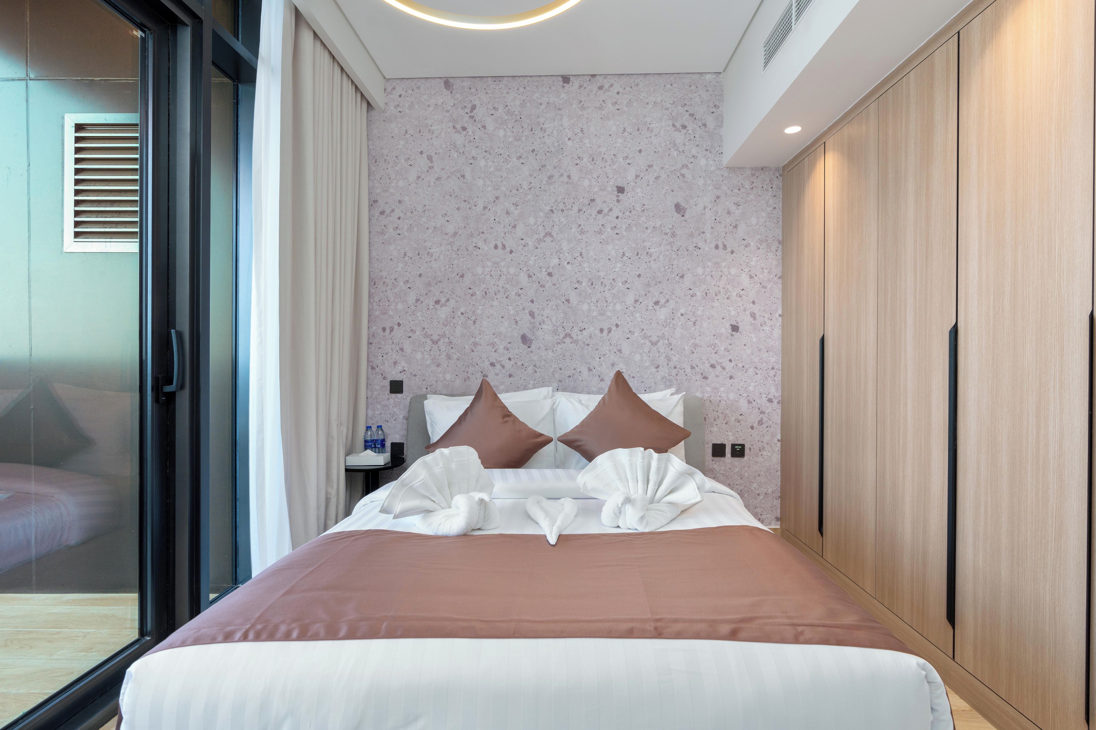 A modern hotel room with a large bed, a sliding glass door, and a built-in wardrobe.