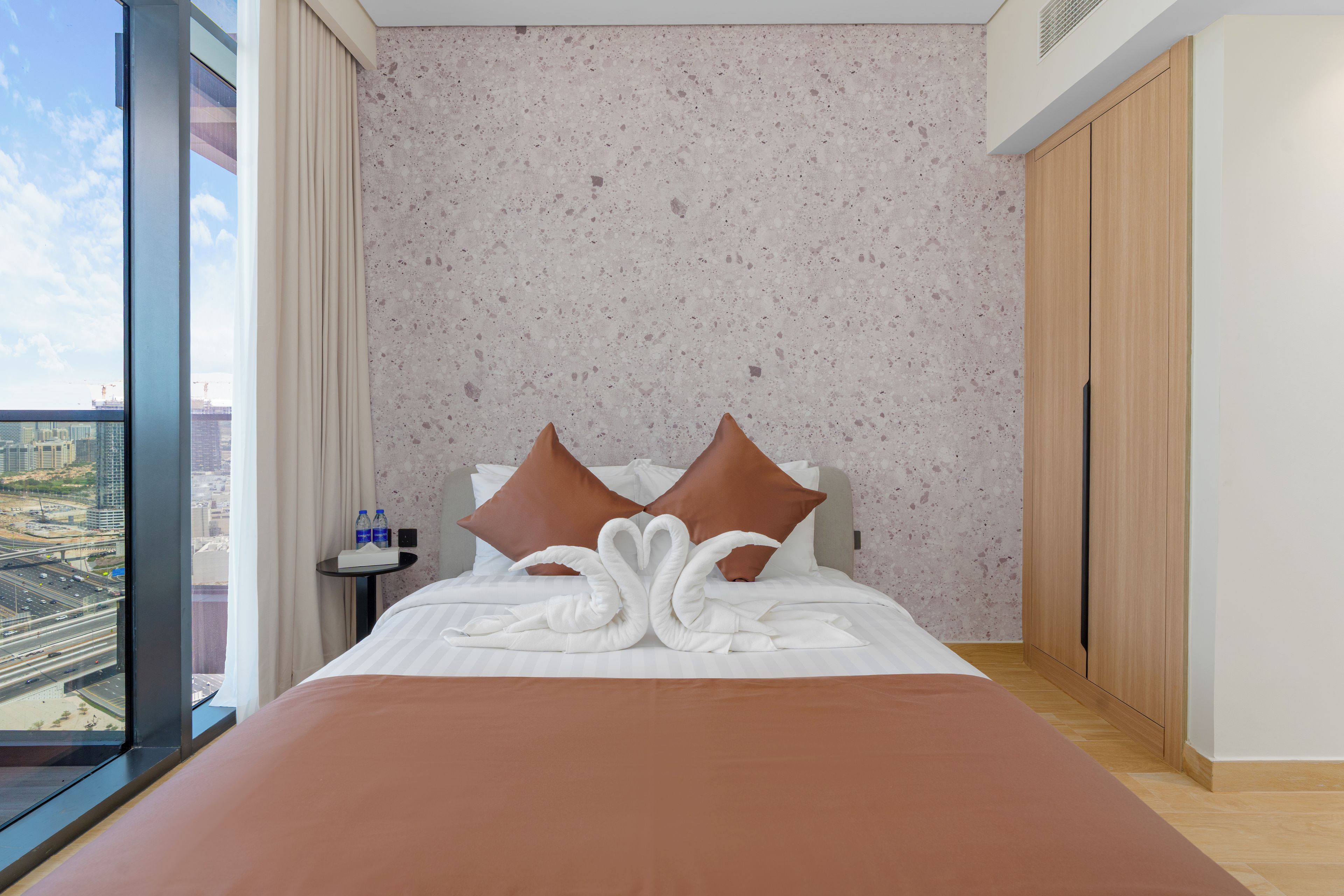 A hotel room with a bed, a view of the city, and a large window.