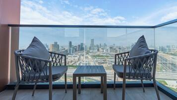 A balcony with two chairs and a small table, overlooking a cityscape with buildings and a highway.