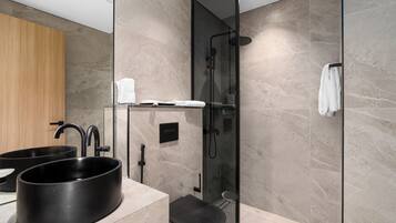 Un baño moderno con ducha envuelta en vidrio, un lavamanos negro y un mueble de tocador de madera.