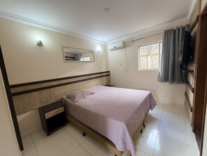 Quarto com cama, mesa de cabeceira, espelho, ar condicionado e janela com cortinas.