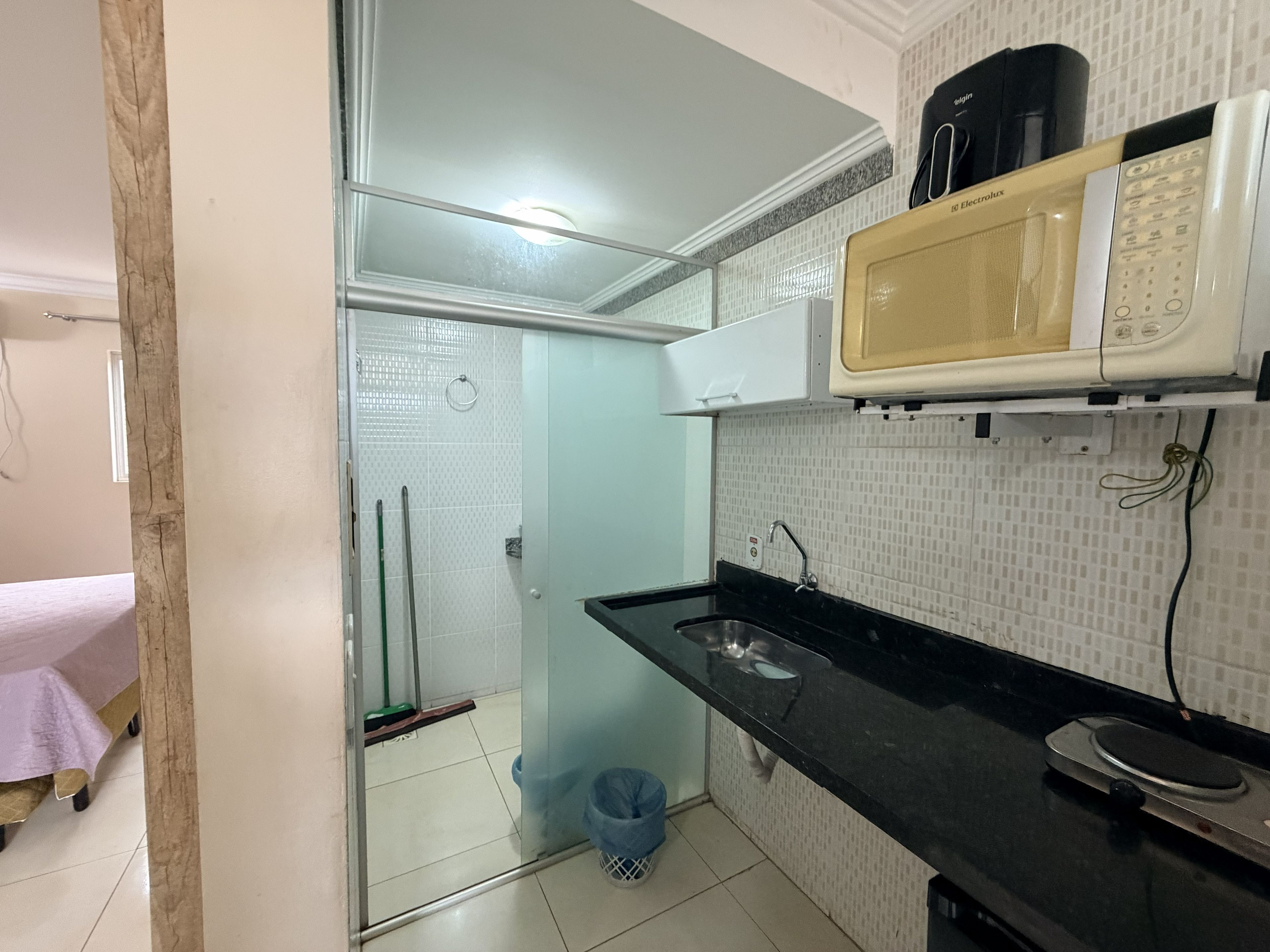 Una cocina compacta con microondas, un lavabo y una escoba en la esquina.