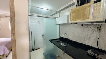 Una cocina compacta con microondas, un lavabo y una escoba en la esquina.