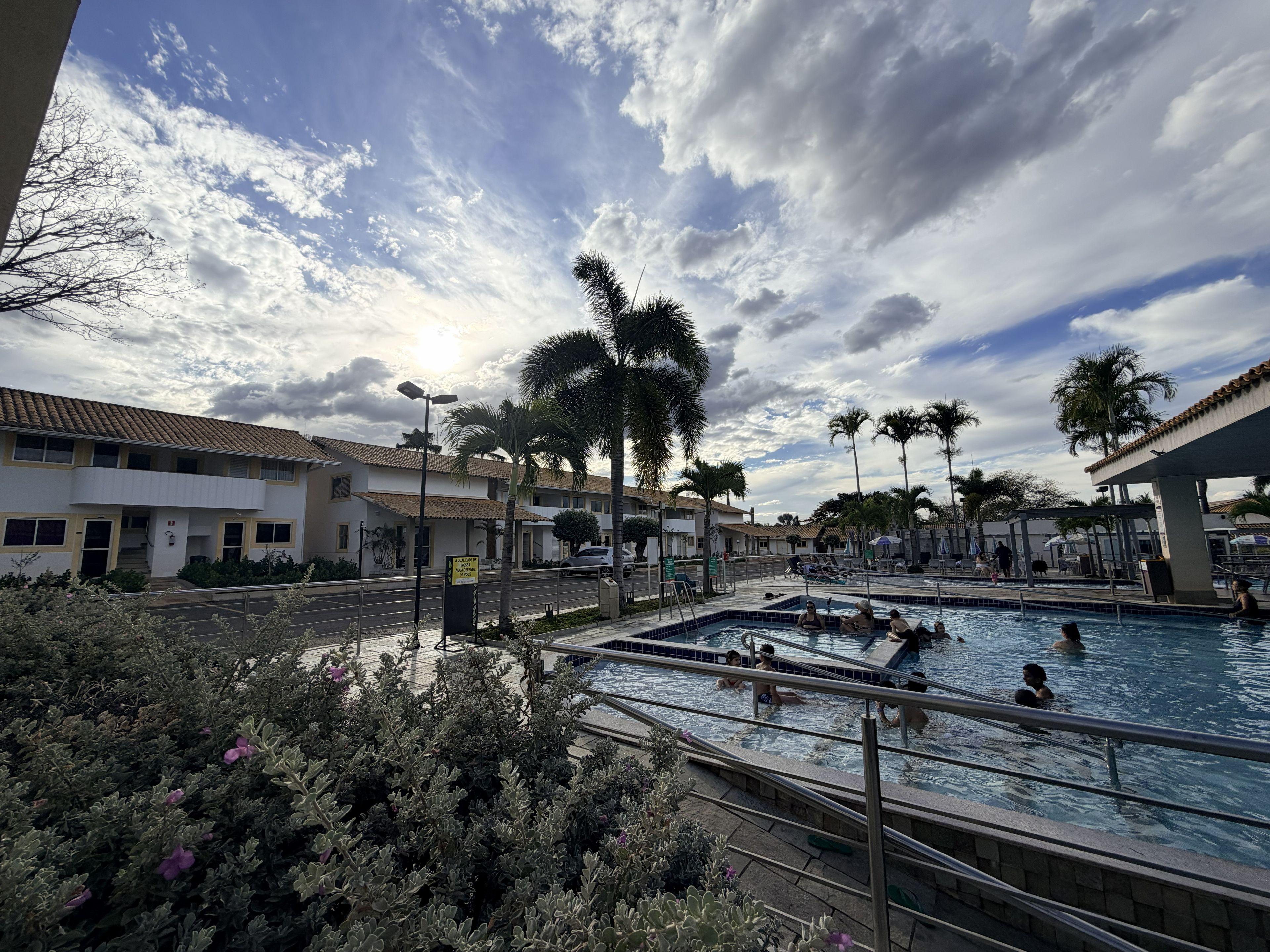 Zona de piscinas con varias albercas, palmeras y un edificio con techo de tejas.