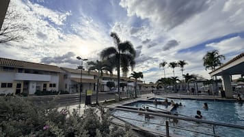 Zona de piscinas con varias albercas, palmeras y un edificio con techo de tejas.