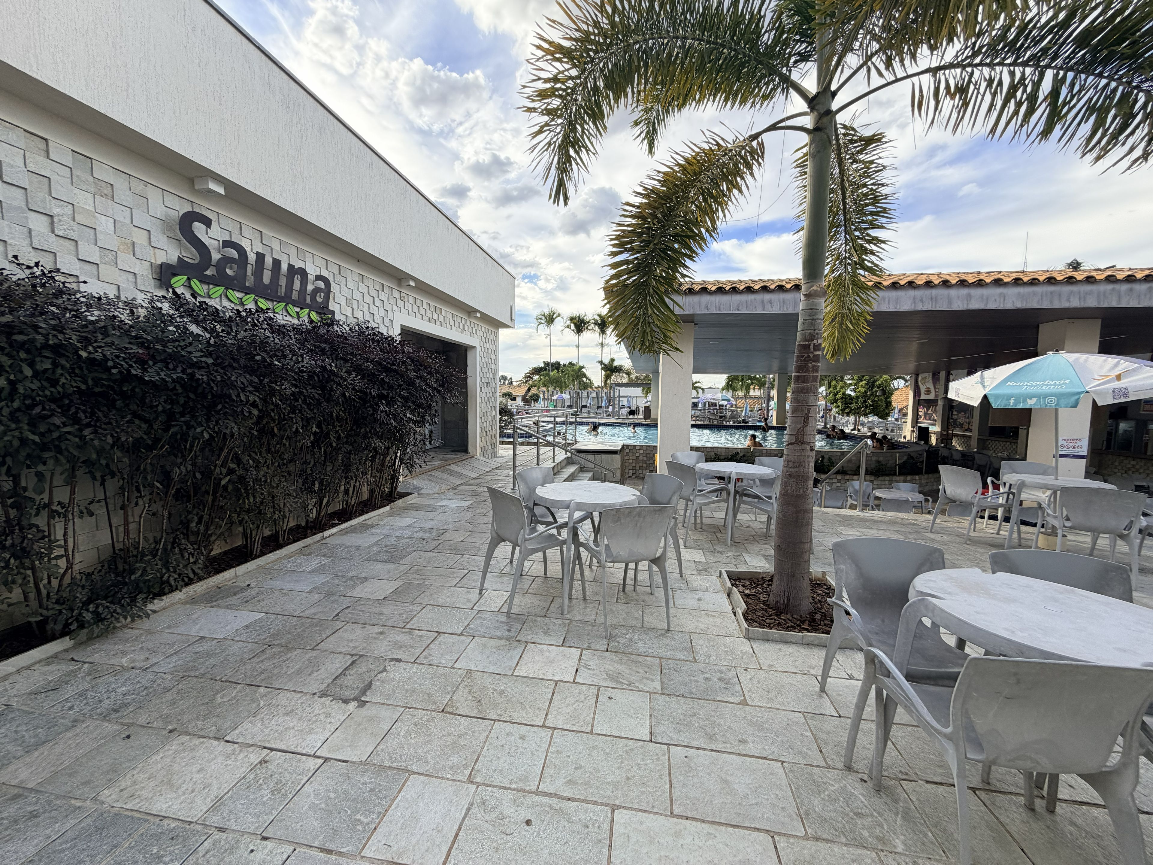 A spa area with a tiled patio, outdoor seating, and a pool in the background.