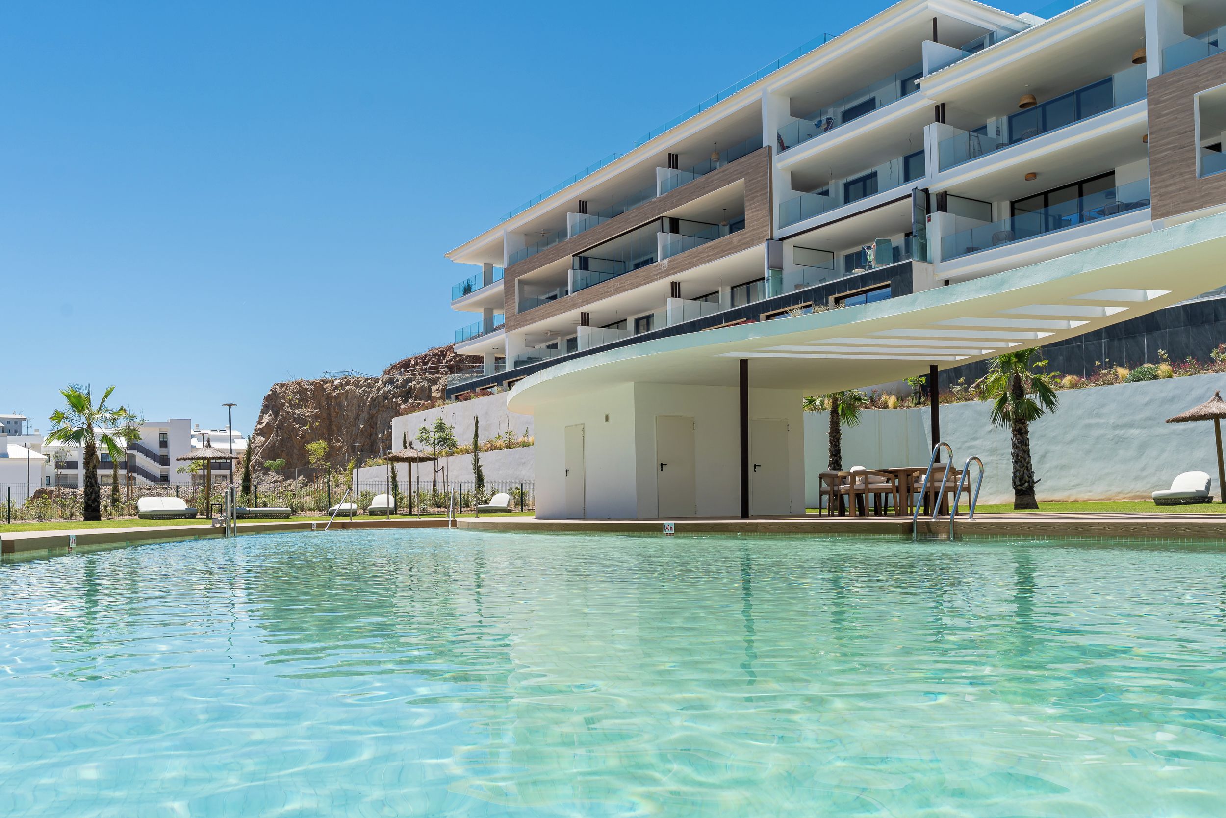 A modern hotel with a pool, multiple balconies, and outdoor seating.