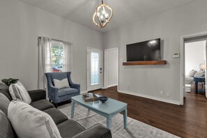 Una sala de estar con sofá, sillón, mesa de centro y televisor de pantalla plana montado en la pared.