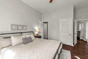 Un dormitorio con cama, mesitas de noche, lámpara y una puerta que da a otra habitación.