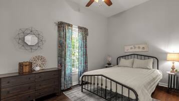Quarto com cama, penteadeira, janela com cortinas e ventilador de teto.