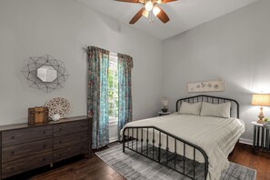 Une chambre à coucher comprenant un lit, une commode, une fenêtre avec des rideaux et un ventilateur de plafond.