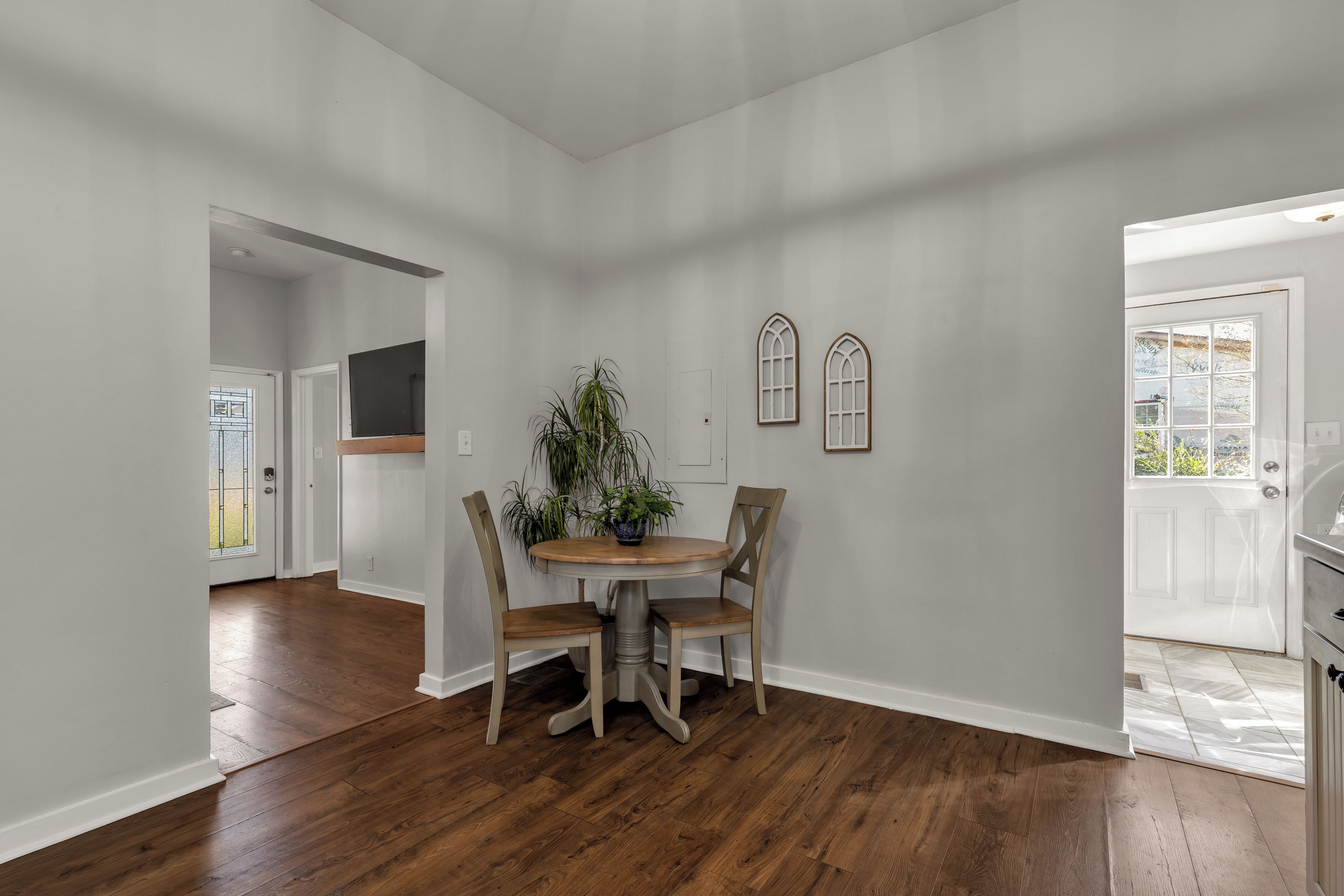A dining area with a wooden table and chairs, a potted plant, and two arched windows.