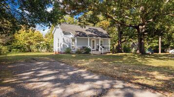A single-story house with a front porch, surrounded by trees and a driveway.