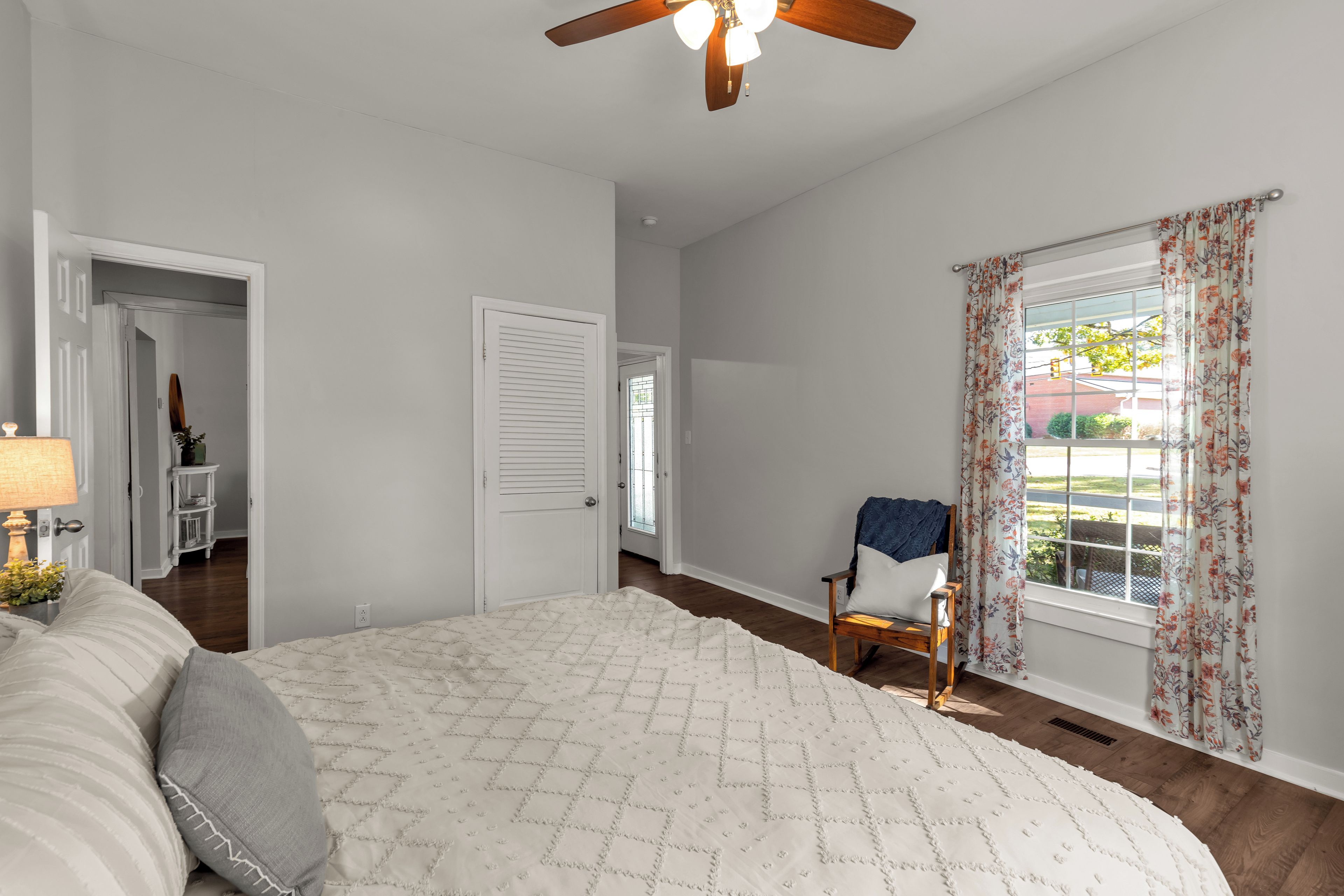 A bedroom with a bed, a chair, a ceiling fan, and a window with curtains.