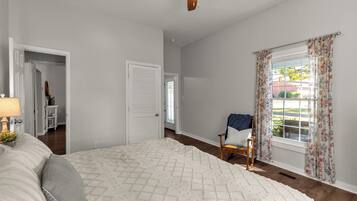 A bedroom with a bed, a chair, a ceiling fan, and a window with curtains.