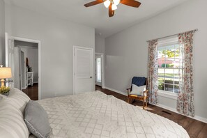 Une chambre à coucher avec un lit, une chaise, un ventilateur de plafond et une fenêtre avec des rideaux.