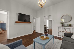 Un salón espacioso con un televisor de pantalla plana montado en la pared, una mesa de centro de madera y un sofá gris.