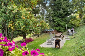 A garden with a fire pit, seating area, and a metal hanging chair. - Laetitia Chalet - Sleeps 8 - Charm and Authenticity (Haute-Nendaz)