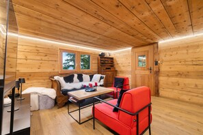 A cozy cabin interior with a wooden ceiling, a sofa, a table, and a chair. - Laetitia Chalet - Sleeps 8 - Charm and Authenticity (Haute-Nendaz)