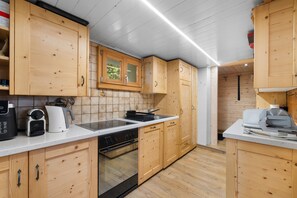 A modern kitchen with wooden cabinets, a built-in oven, and a countertop with appliances. - Laetitia Chalet - Sleeps 8 - Charm and Authenticity (Haute-Nendaz)